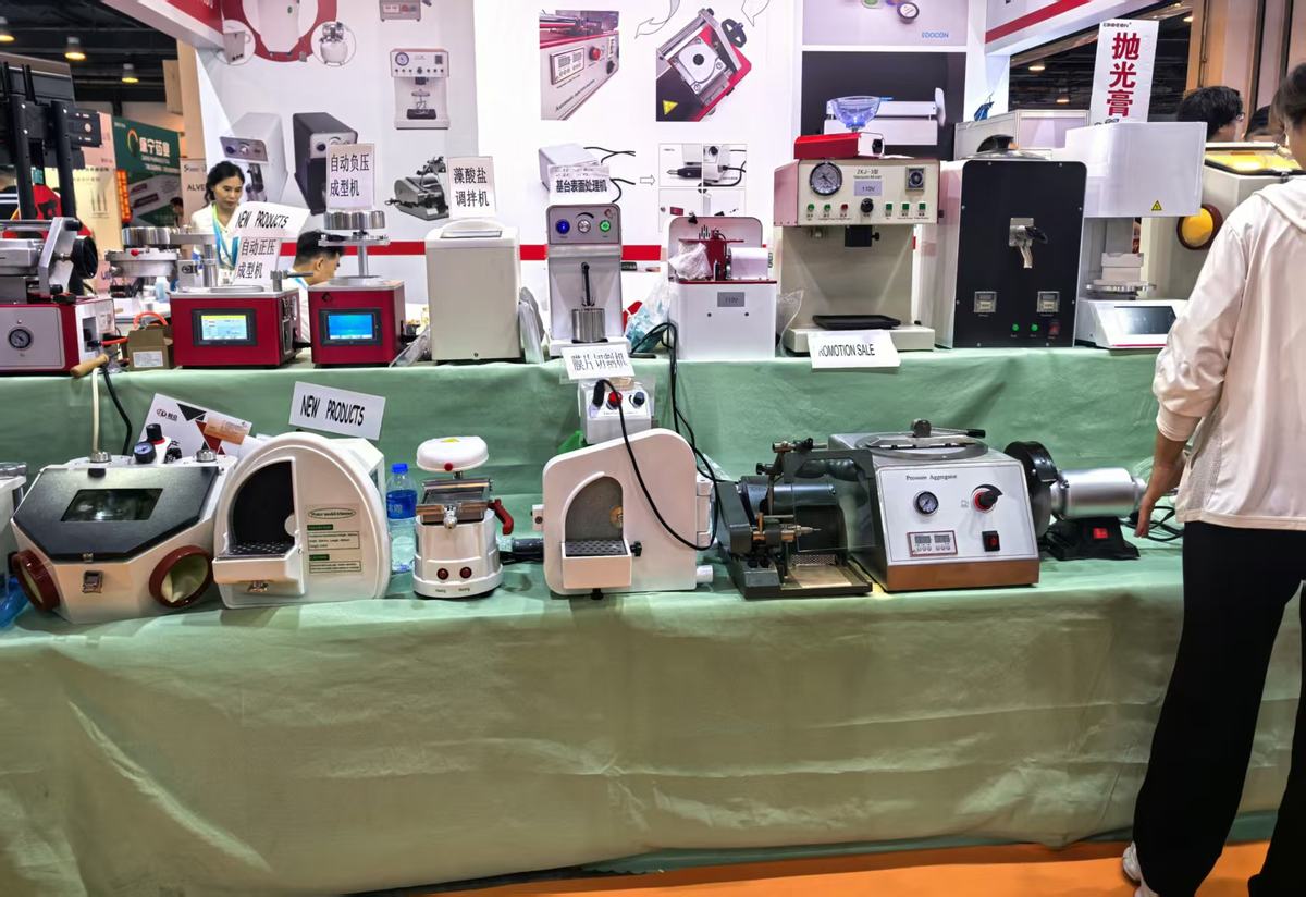 Trade show bench with benchtop dental lab machines on a green cloth; the abutment surface treatment unit carries a 110V label